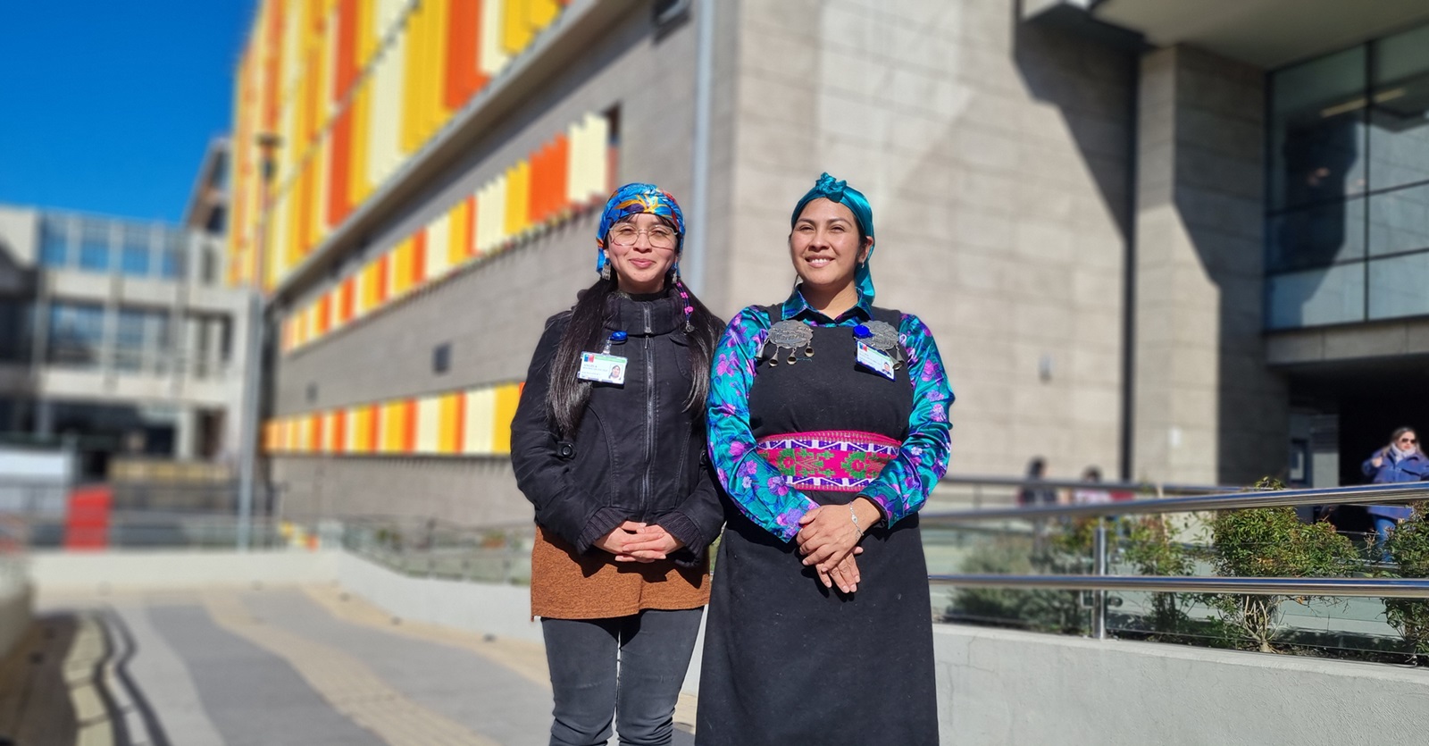 dos mujeres con elementos de vestimenta mapuche frente al hospital